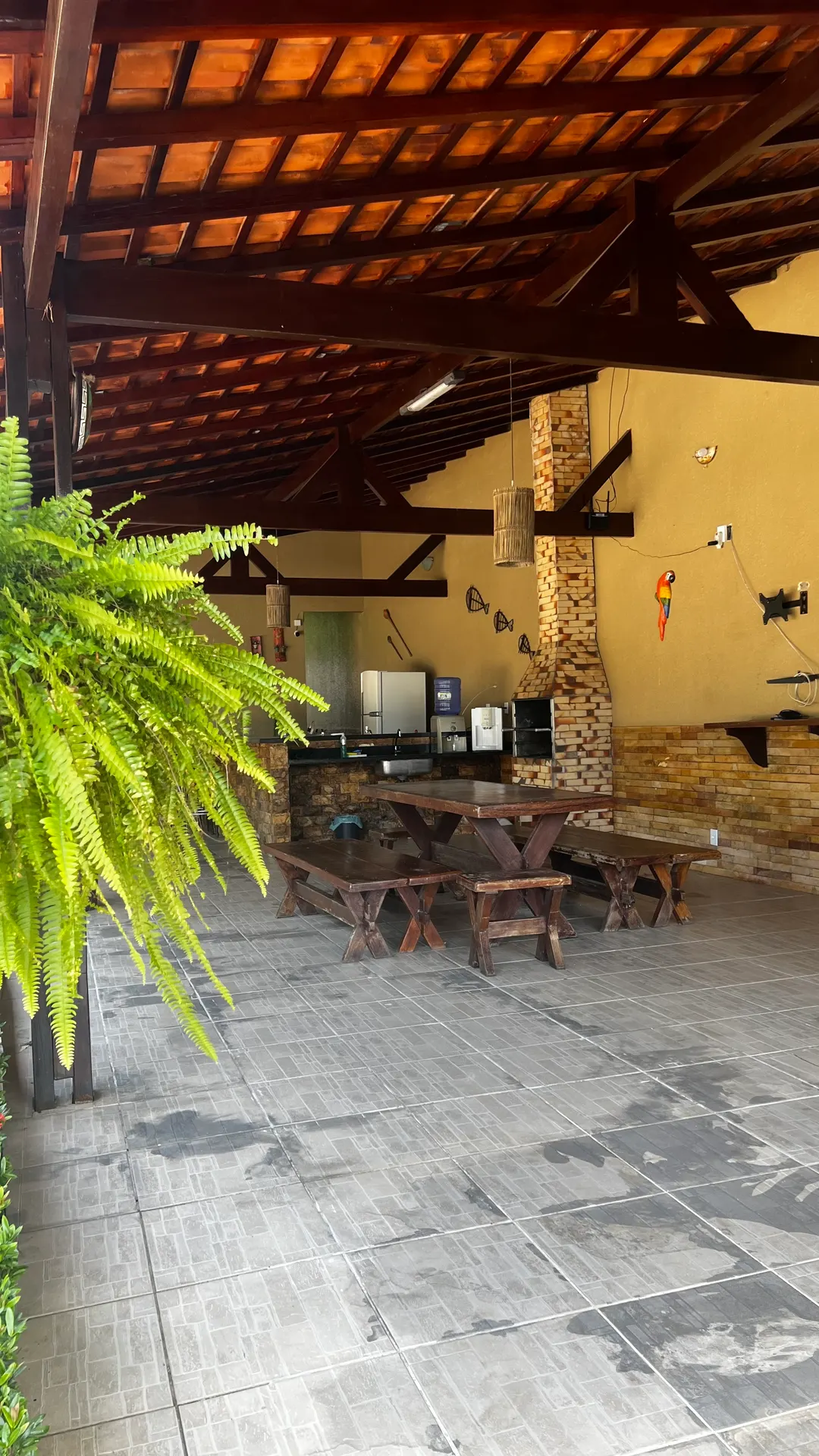 Área gourmet coberta com mesas rústicas de madeira e samambaia